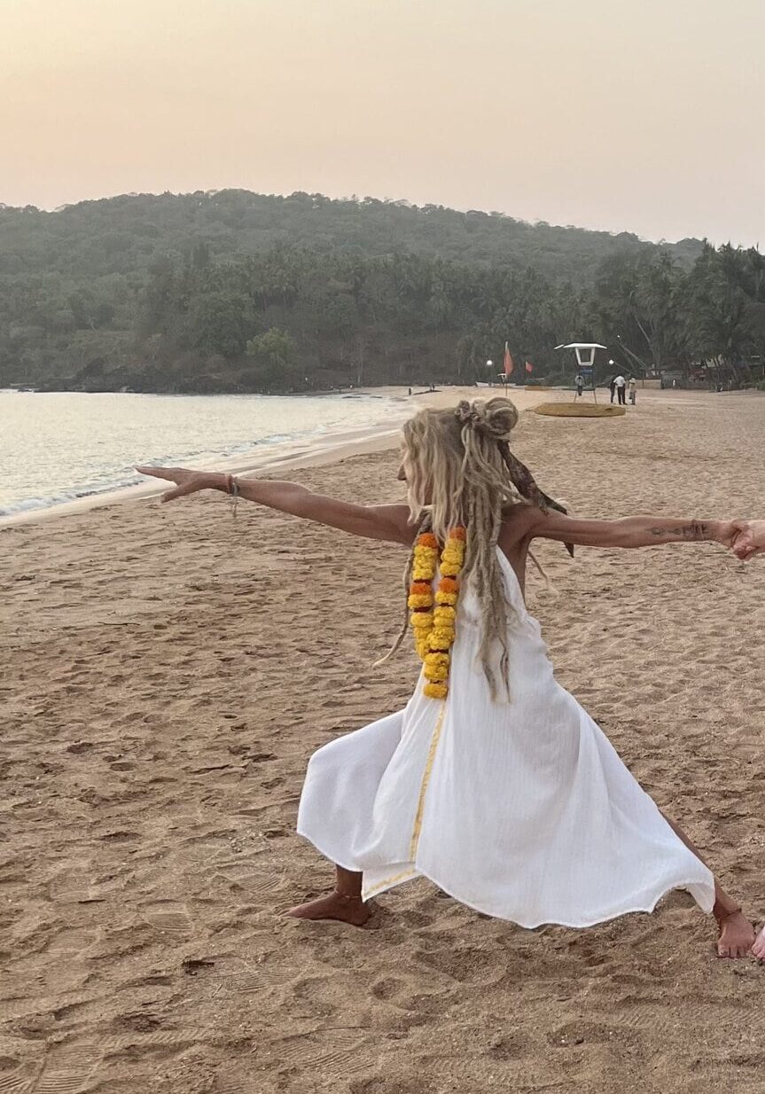 Woman practicing yoga on a Welsh beach at sunset with arms outstretched.